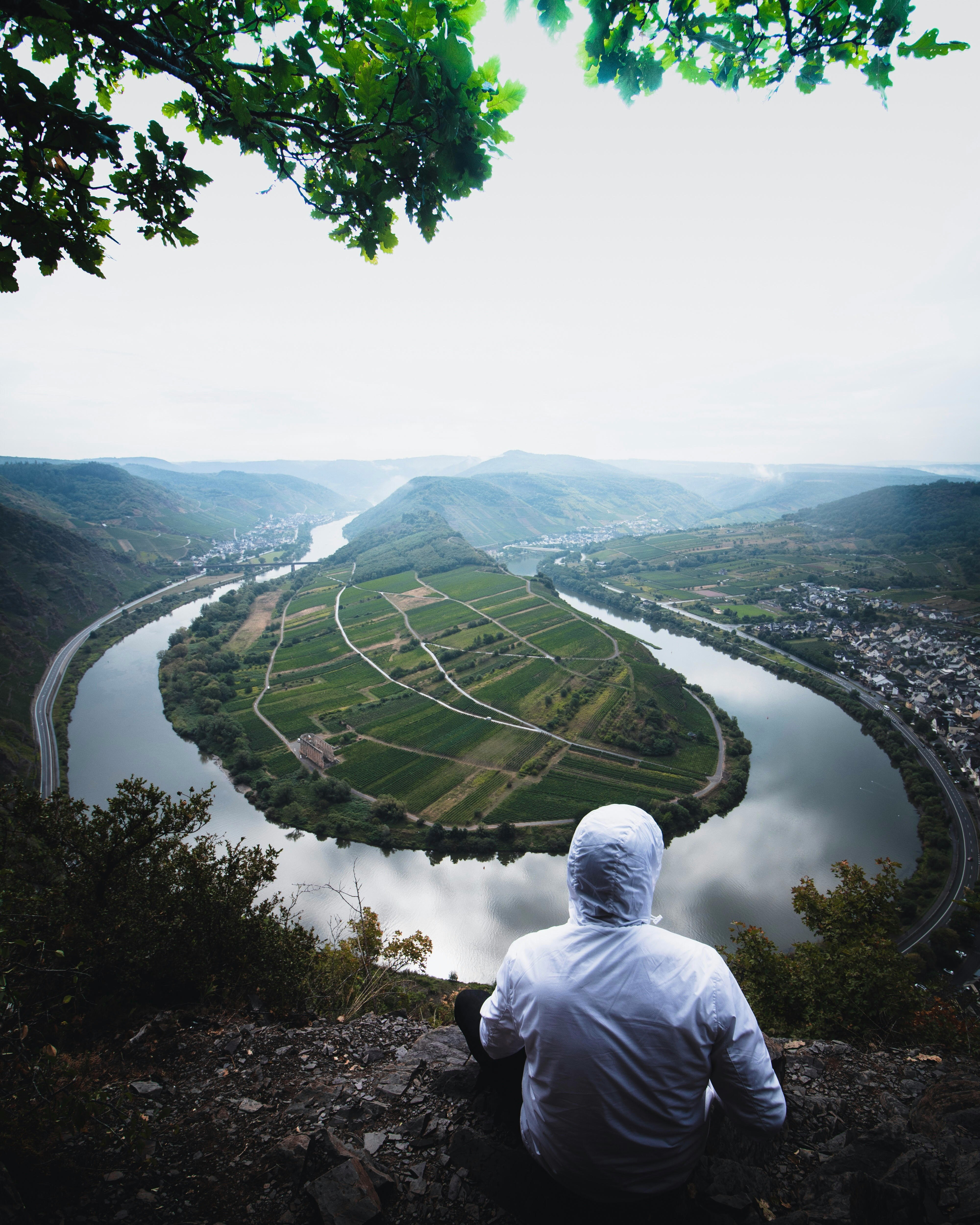 man in white hoodie sitting on rock looking at river
